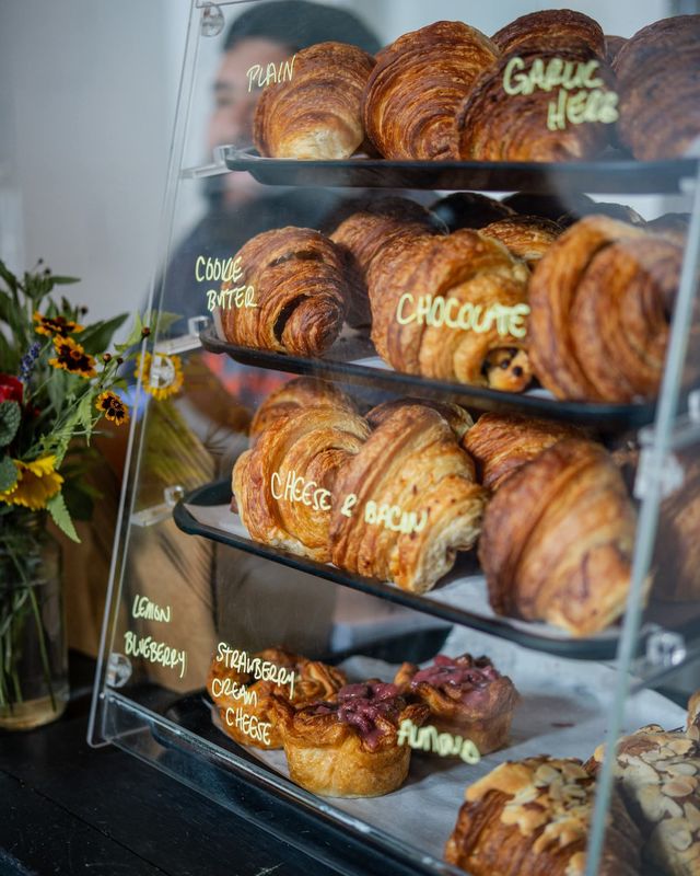 A glass pastry case stacked with croissants labeled in chalk