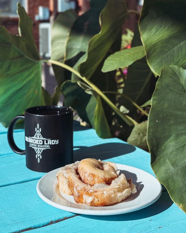 A black Bearded Lady mug and a glazed pastry on a teal patio table