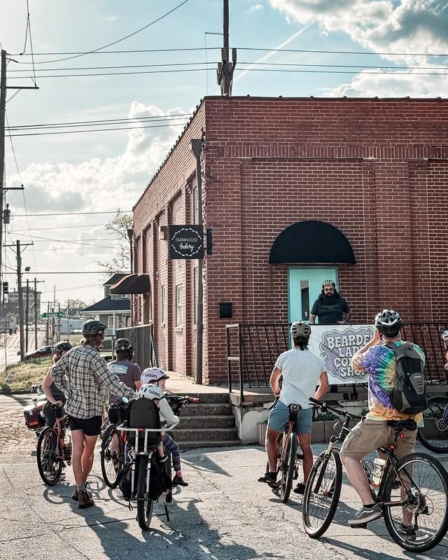 A group on bicycles gathered outside the brick coffee shop on a sunny street